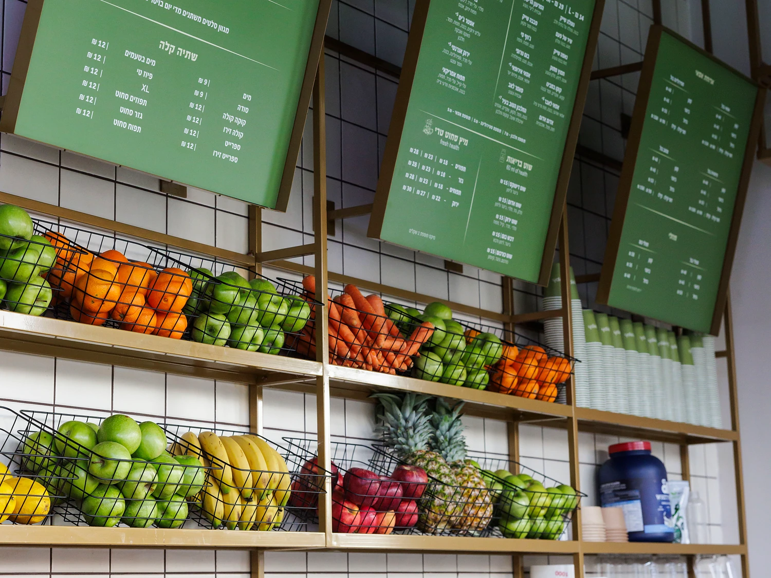 קיר הפירות בסניף JUICEPH: סלסלות תפוזים, תפוחים, גזר ובננות מתחת ללוחות התפריט