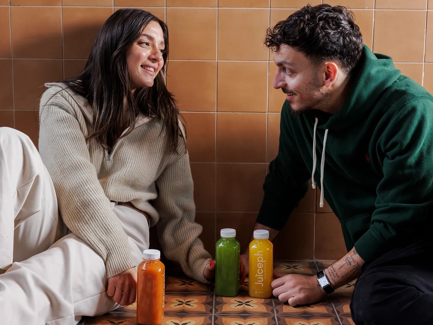 זוג צוחק עם בקבוקי מיצים של JUICEPH על רצפת אריחים