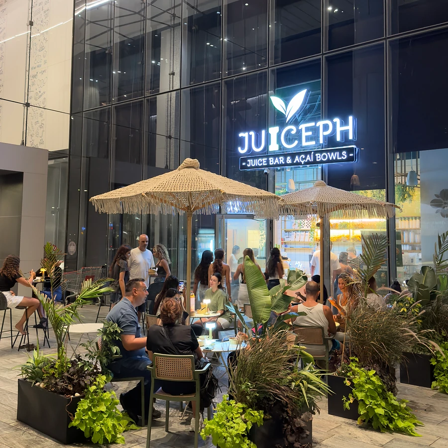 המרפסת של JUICEPH חולון בערב, עם שמשיות ואנשים