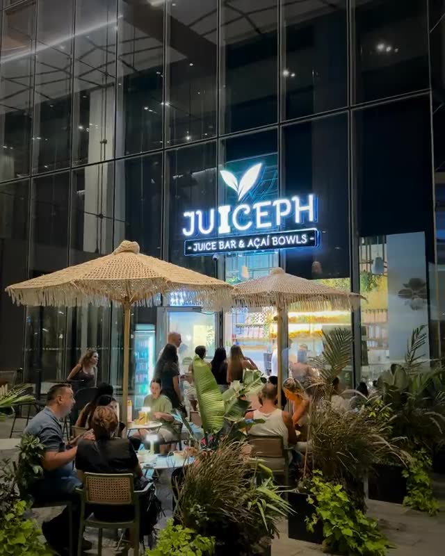 סניף JUICEPH בערב: שלט הניאון, שמשיות ולקוחות יושבים בחוץ